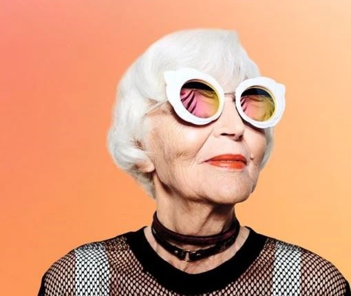 Lächelnde ältere Dame mit stylischer Sonnenbrille, Lederhalsband und Netzshirt, Karriere Symbolbild,