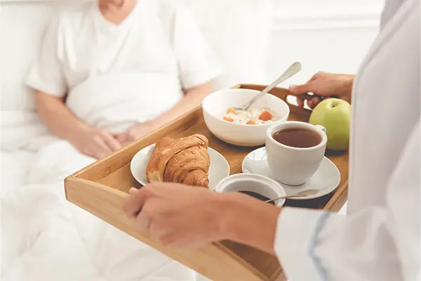 Aufenthalt in der Klinik, Patient in Krankenhausbett, Frühstückstablett wird am Bett serviert