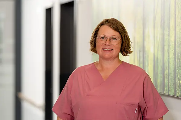 Porträt der Leiterin der Physiotherapie in altrosa Pflegeoberteil vor unscharfem Hintergrund