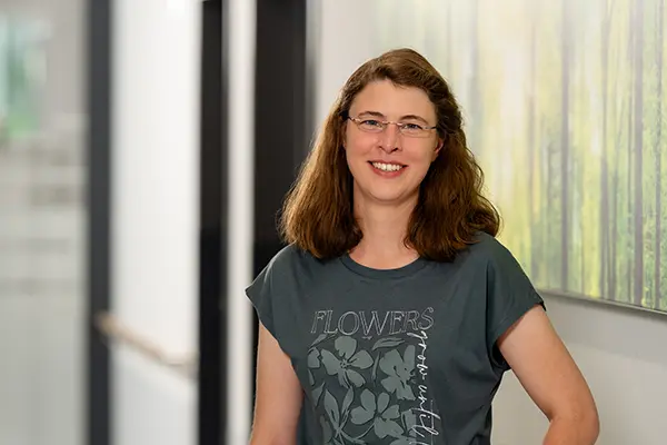 Porträt von der Sozialdienstleiterin in einem khaki T-Shirt mit Blumenmotiv vor unscharfem Hintergrund